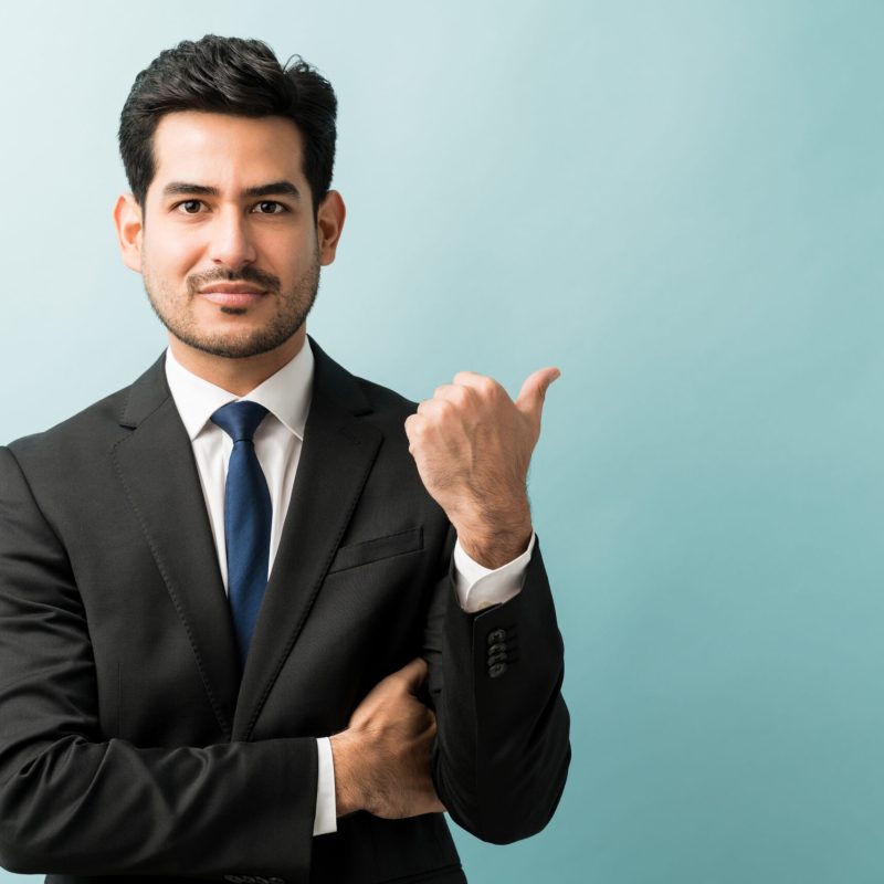 Hispanic male executive gesturing at copy space while making eye contact in studio